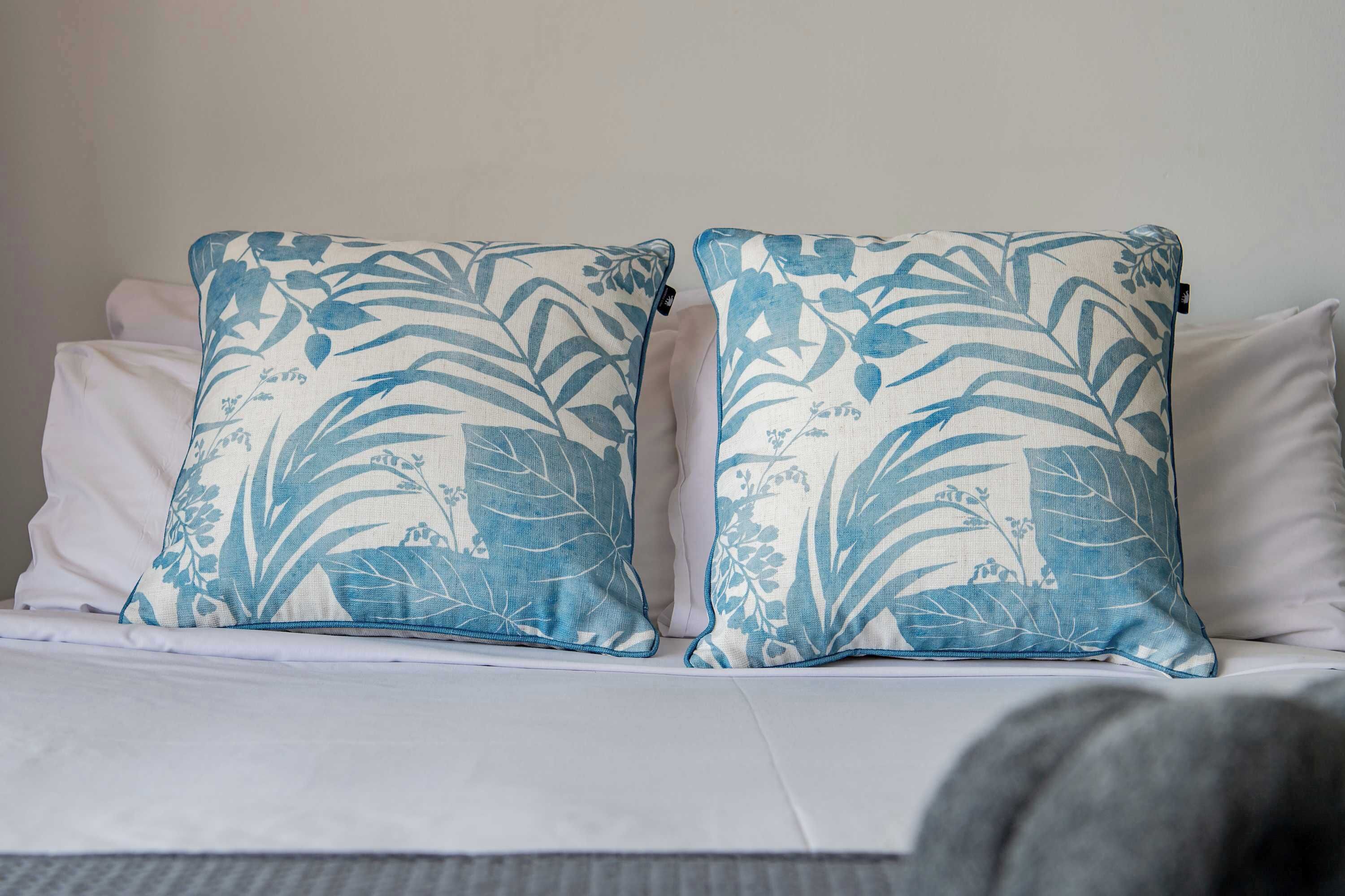 A bed with two pillows featuring a blue and white leaf pattern.