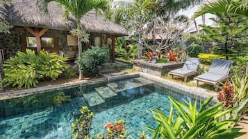 Une piscine entourée d’une végétation luxuriante et bordée d’une structure au toit de chaume.