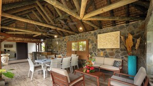 A spacious outdoor seating area with stone walls, wooden furniture, and a ceiling fan.