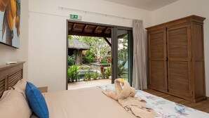 A bedroom with a bed, a wooden wardrobe, and a view of a garden through an open door.