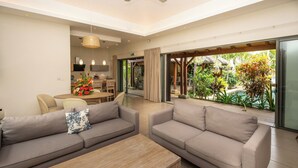 A modern living room with a sofa, coffee table, and a view of a lush garden through large glass doors.