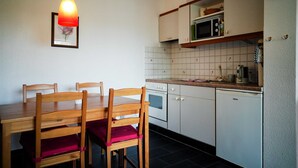 A kitchen with a wooden dining table, chairs, a microwave, and a clock on the wall. - Vacation apartment Rosenstube - Lindenhof (Steinberg)