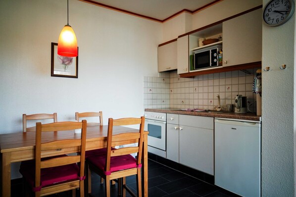 A kitchen with a wooden dining table, chairs, a microwave, and a clock on the wall. - Vacation apartment Rosenstube - Lindenhof (Steinberg)