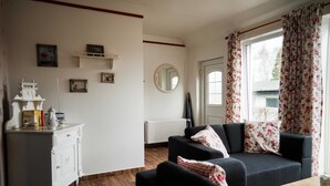 A living room with a sofa, a small table, a white cabinet, and a window with floral curtains. - Vacation apartment Rosenstube - Lindenhof (Steinberg)