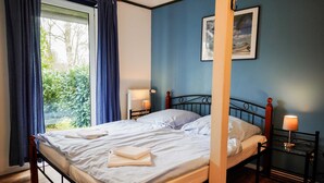 A four-poster bed with white linens, two bedside tables with lamps, and a window with curtains. - Vacation apartment Rosenstube - Lindenhof (Steinberg)