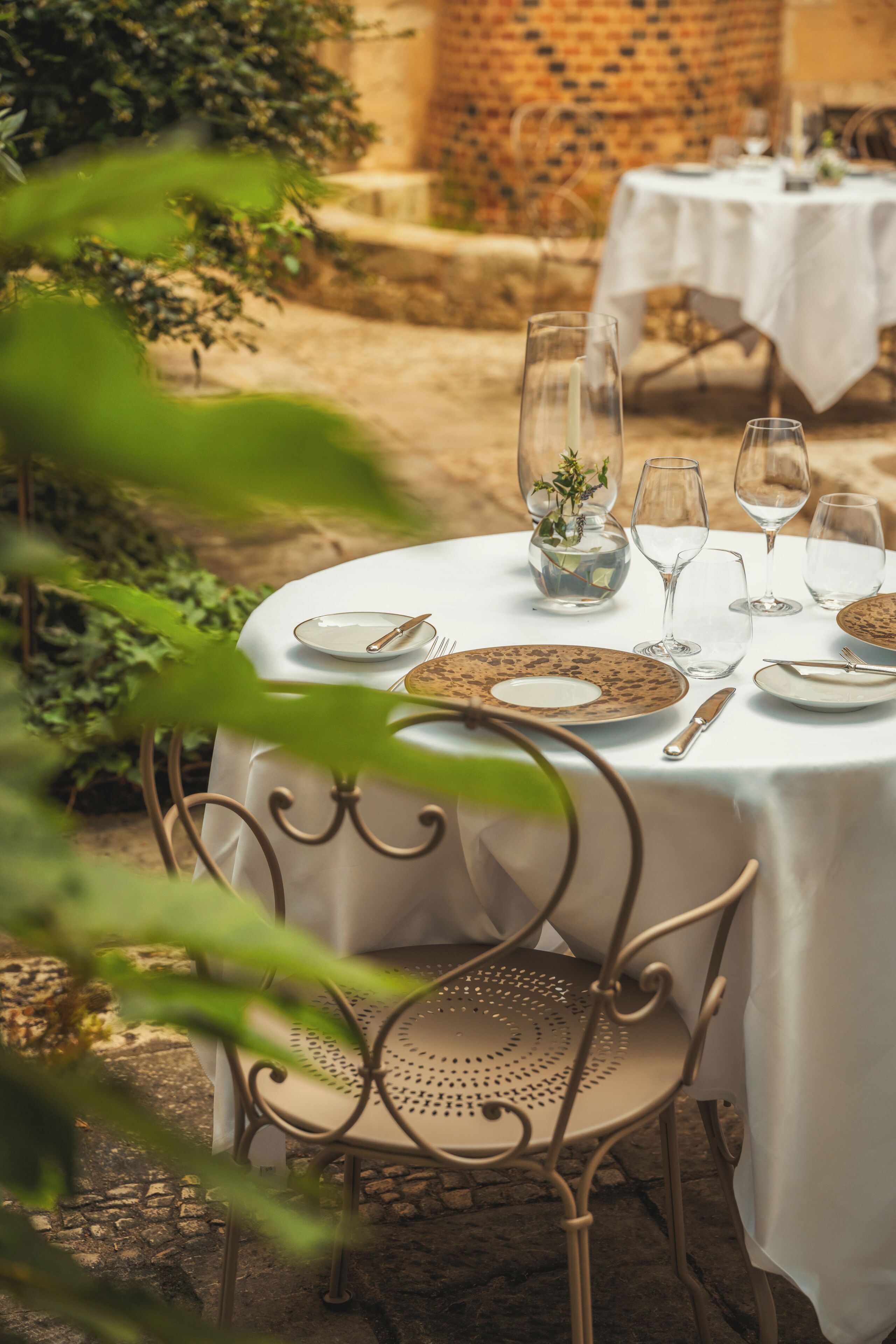 Mesa redonda preparada para comer al aire libre, con platos, cubiertos y vasos.