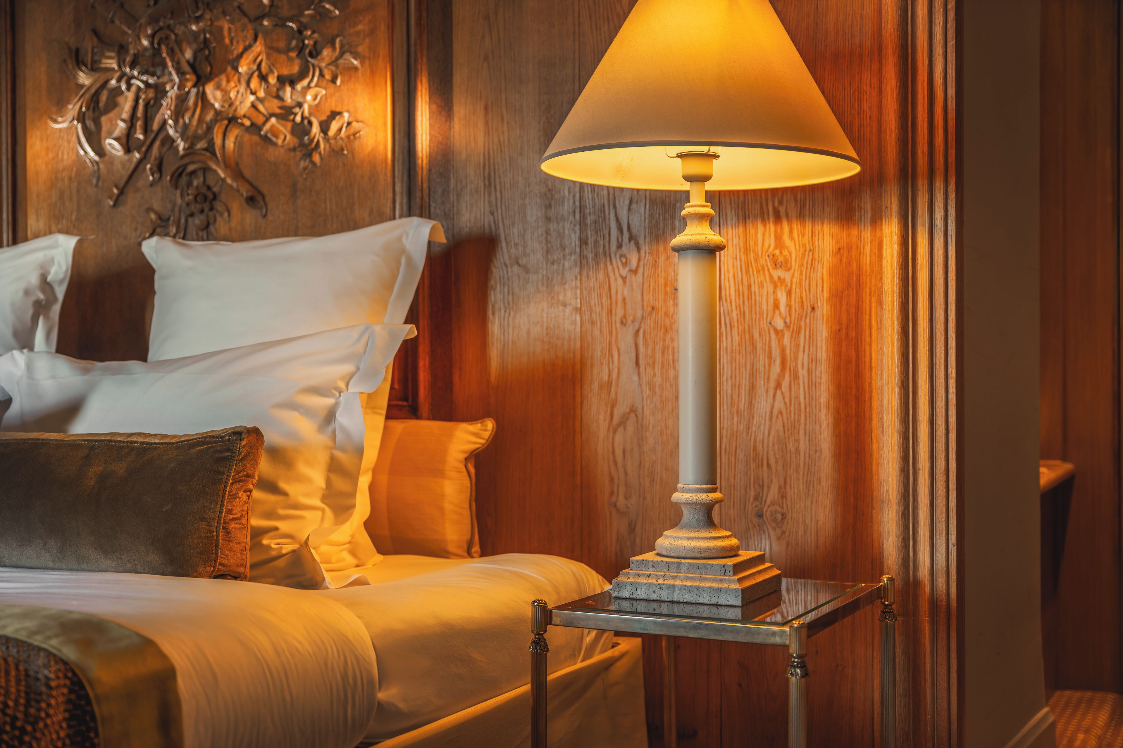 A neatly made bed with pillows and a bedside table with a lamp.