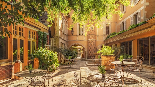 An outdoor courtyard with stone flooring, metal tables and chairs, and greenery.