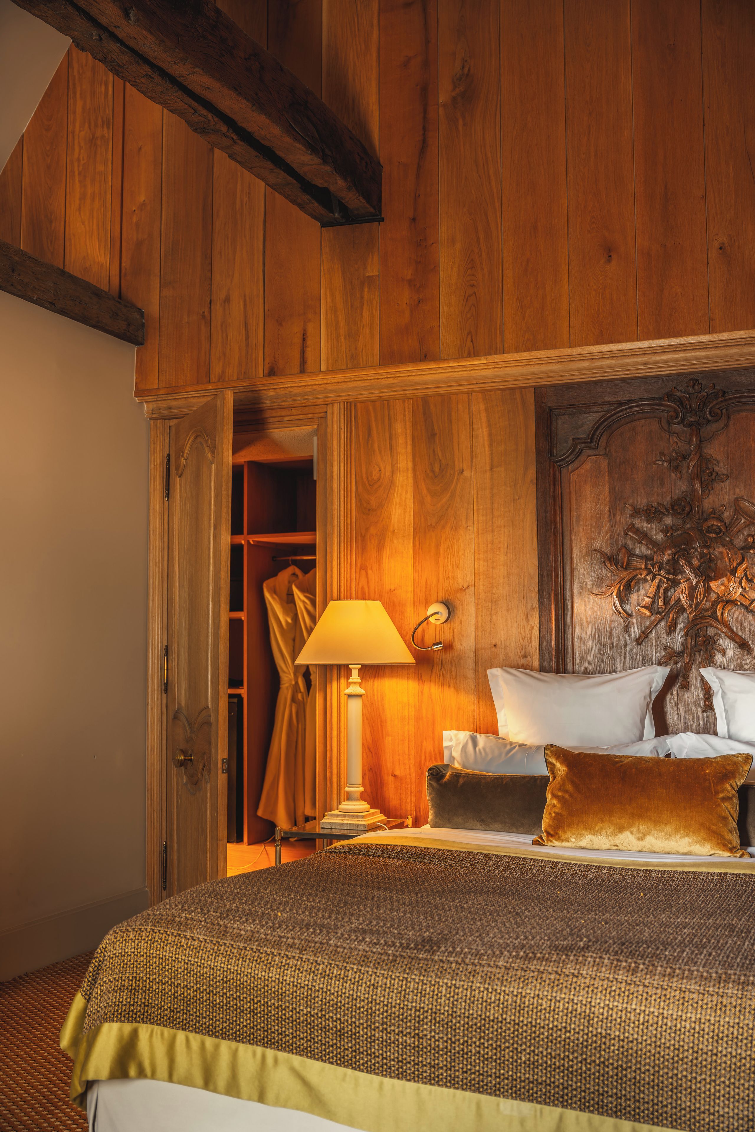 Een slaapkamer met houten lambrisering, een bed, nachtkastje, lamp en een kledingkast.