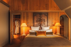 A bedroom with a large bed, two bedside lamps, a wooden headboard with a carved tree, and a robe hanging on a door.