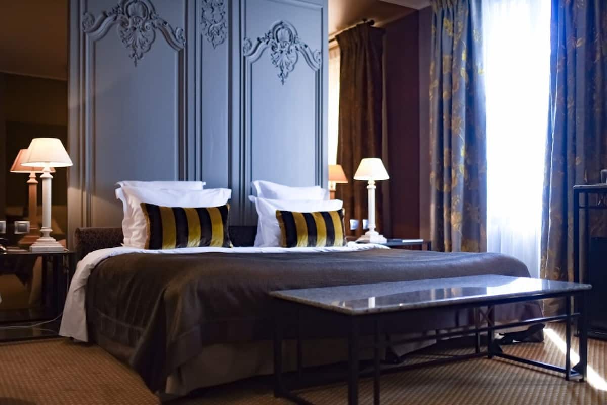 Une chambre d’hôtel avec un grand lit, deux tables de chevet, une petite table et un miroir.