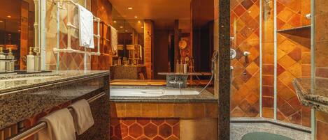 A modern bathroom with a granite countertop, a large mirror, a shower with a glass door, and a green bench.