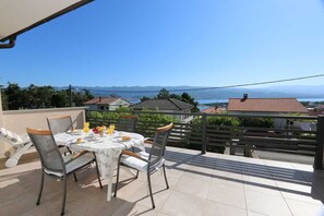 A terrace with a table set for breakfast, chairs, and a view of the sea and mountains. - Apartment Skvicalo (Silo - island Krk)