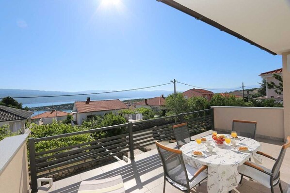 A terrace with a table set for breakfast, overlooking a coastal landscape.