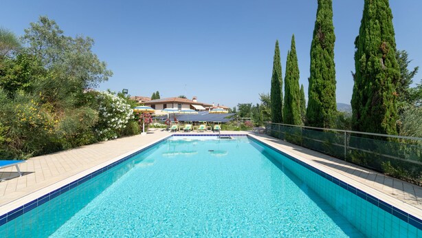 Une piscine rectangulaire à l’eau d’un bleu limpide, entourée d’une terrasse carrelée et d’une rambarde en métal.