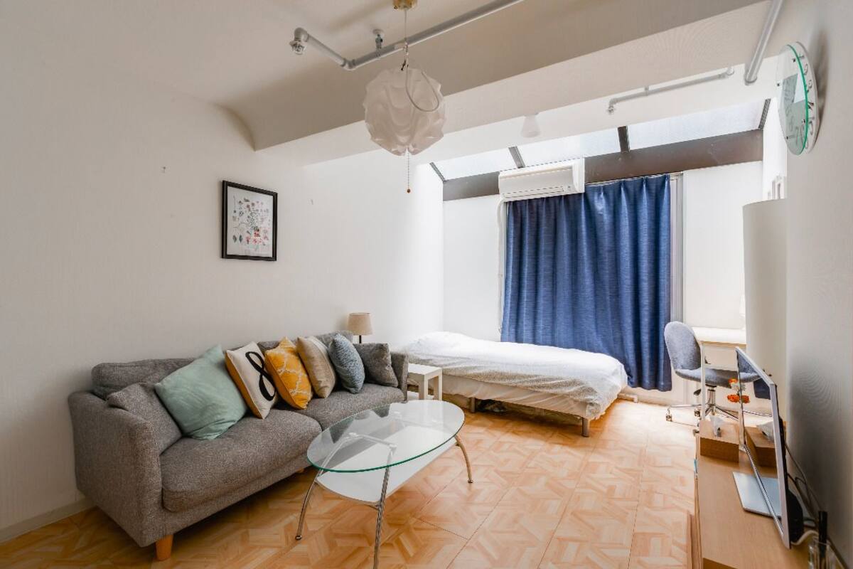 Habitación compacta con sofá, una mesa de vidrio, cama, escritorio y ventana con cortinas.