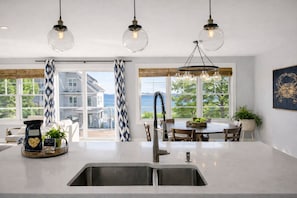 A modern kitchen with a large island, stainless steel sink, and pendant lighting.
