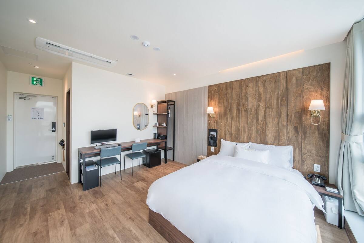 A hotel room with a large bed, a desk with a chair, a television, a mirror, and a wooden accent wall.