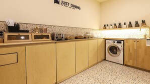 Et lille køkken med en brødrister, en vaskemaskine, og et skilt med teksten "JUST DINING NO REST. NO LIFE".