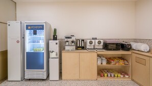 Et tekøkken med køleskab, kaffemaskine, mikroovn og et skab med snacks.