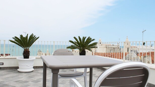 A rooftop terrace with a table and chairs, potted plants, and a view of the sea and buildings. - Estlevante B&B (Vieste)