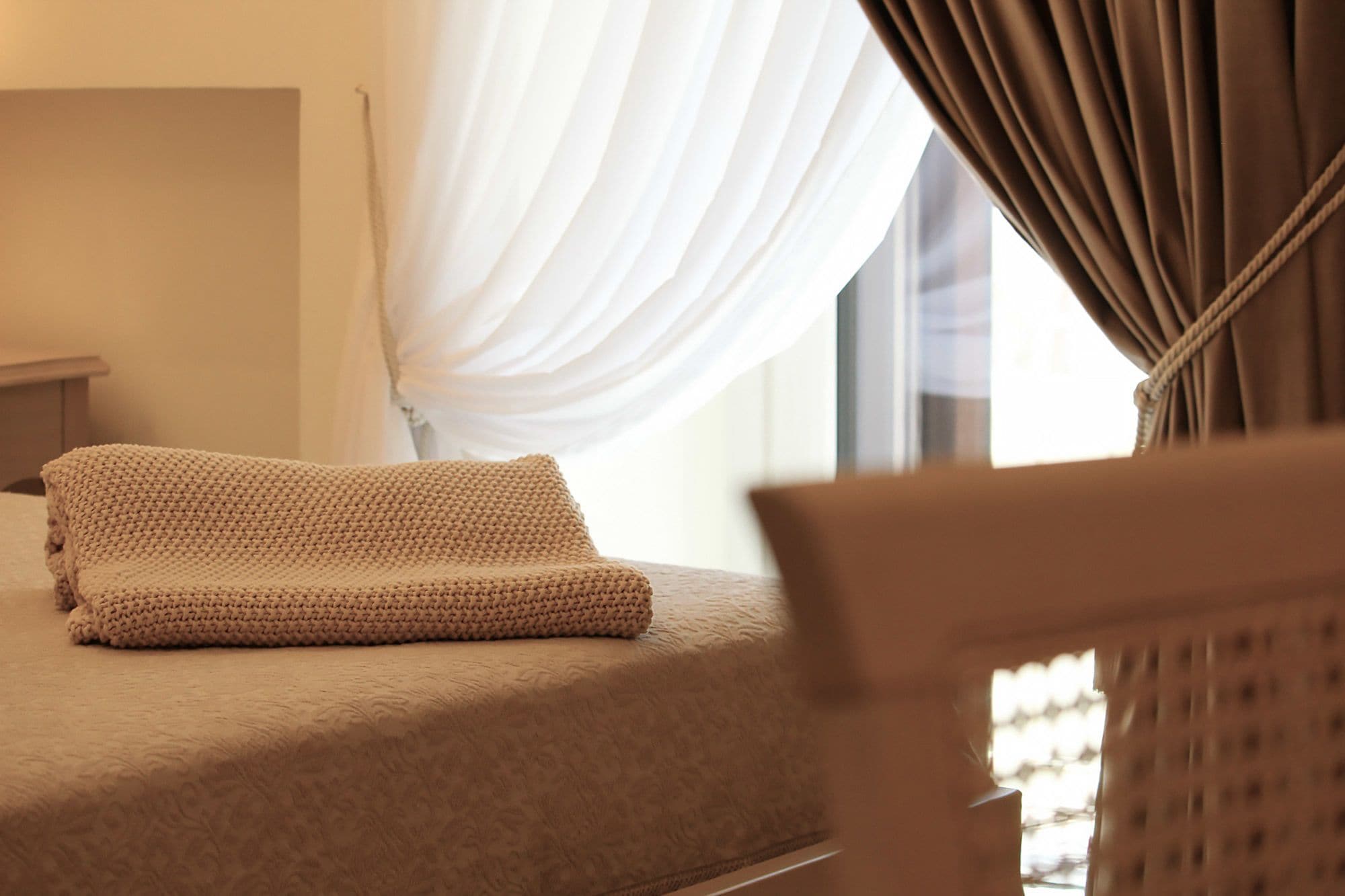 A neatly made bed with a textured blanket, a bedside table, and a window with curtains.