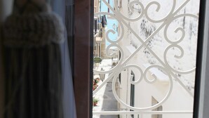 A view through a window with ornate metal bars, a narrow street with buildings, and a glimpse of a balcony with potted plants. - Estlevante B&B (Vieste)