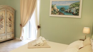 A bedroom with a bed, a painting of a coastal landscape, a lamp, and a vintage cabinet. - Estlevante B&B (Vieste)
