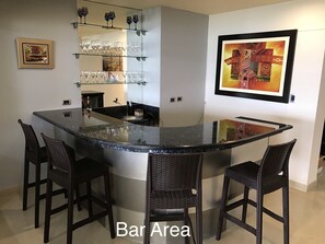 A bar area with a curved granite countertop, four wicker bar stools, and a glass display shelf with wine glasses. - 15th_16th Floor Duplex-A_C & Spectacular Ocean Views Across from Parque del Amor (Miraflores)