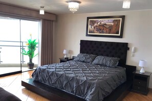 A bedroom with a large bed, a potted plant, a chandelier, a painting, and a sliding glass door. - 15th_16th Floor Duplex-A_C & Spectacular Ocean Views Across from Parque del Amor (Miraflores)