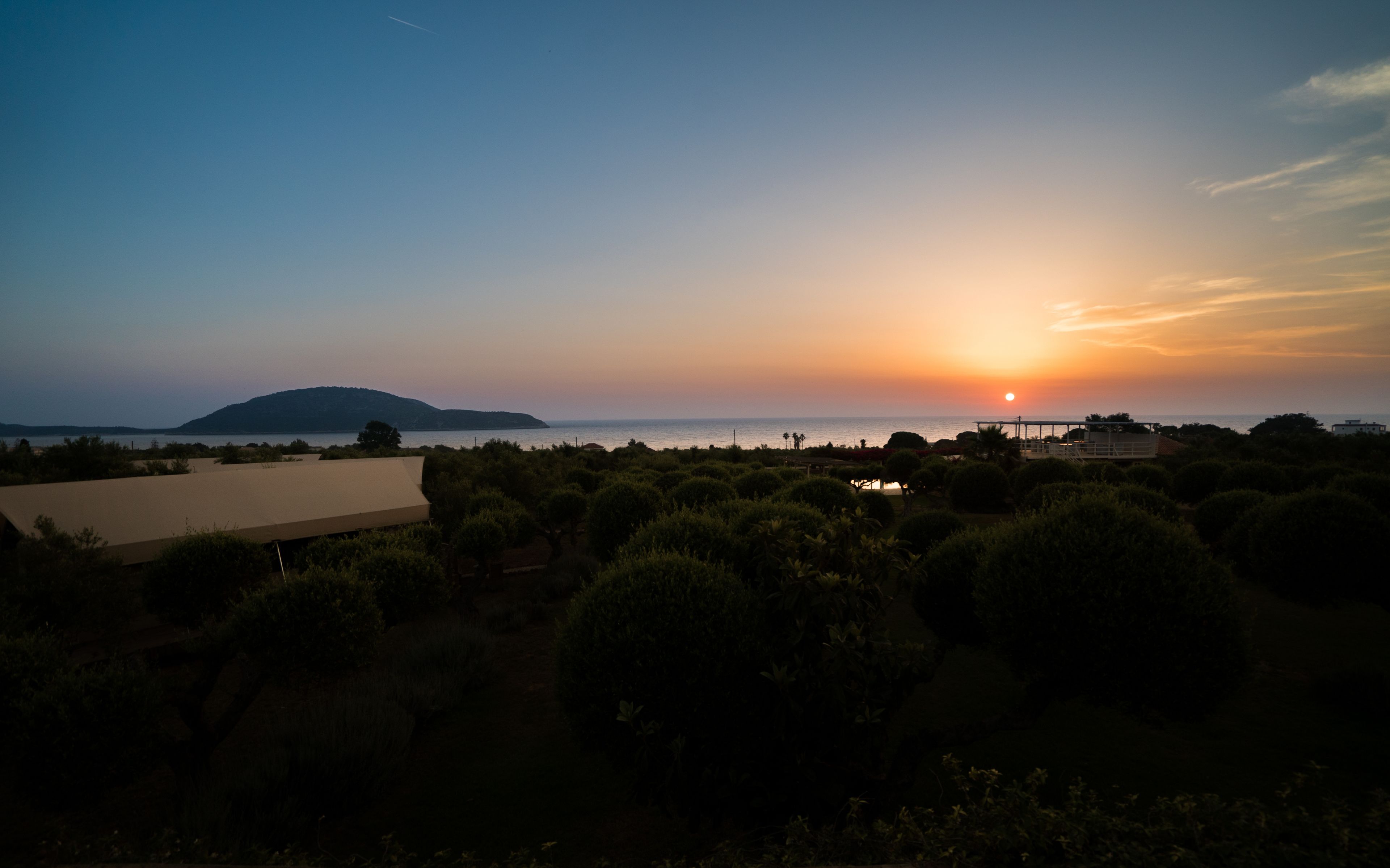 A sunset view over a coastal area with a building and greenery in the foreground.