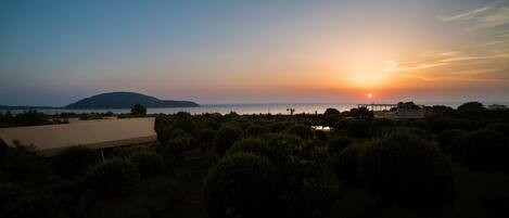A sunset view over a coastal area with a building and greenery in the foreground.