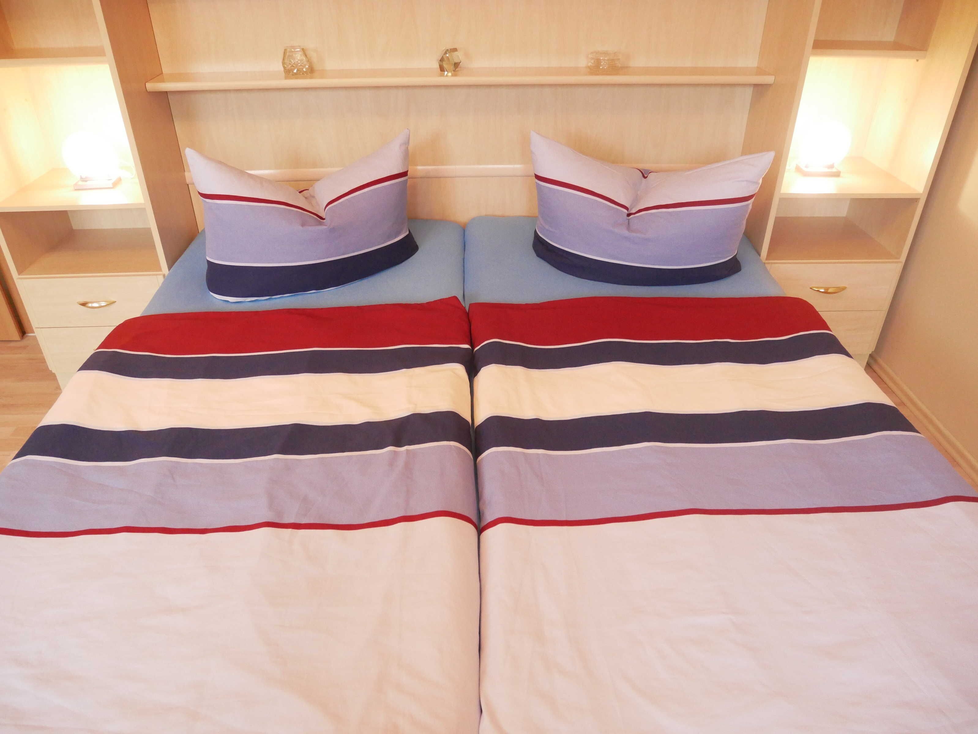 Cama doble con ropa de cama a rayas y almohadas a juego, flanqueada por mesitas de noche con lámparas.