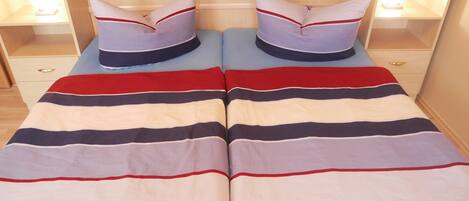 Cama doble con ropa de cama a rayas y almohadas a juego, flanqueada por mesitas de noche con lámparas.
