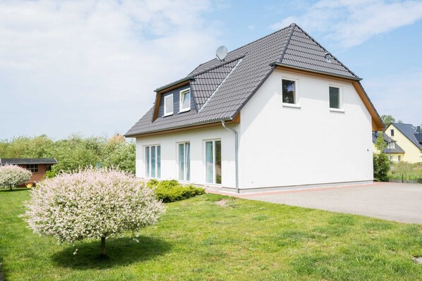 A modern two-story house with a sloped roof, large windows, and a satellite dish.