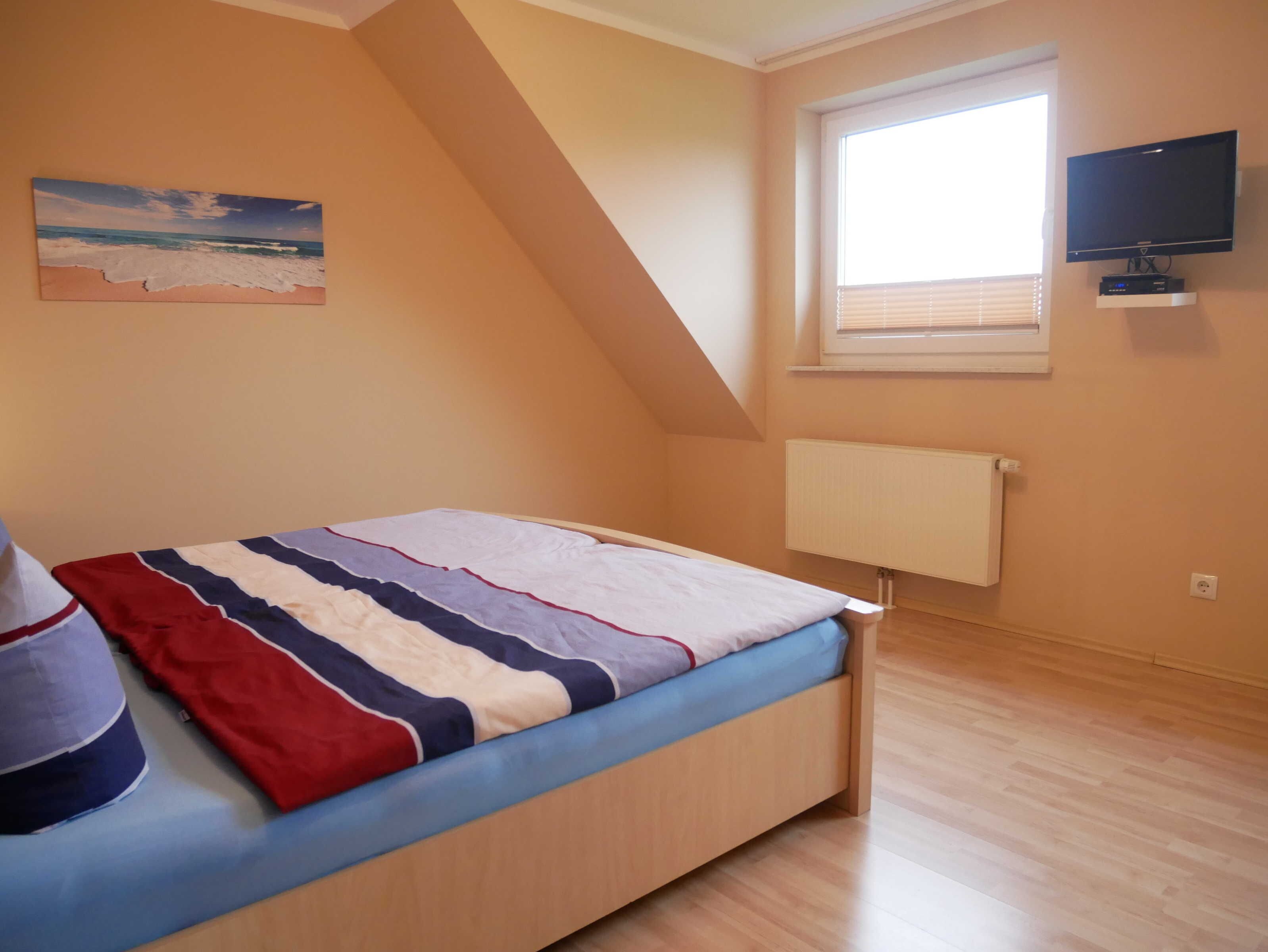 A bedroom with a bed, a painting, a window with blinds, a TV, and a radiator.