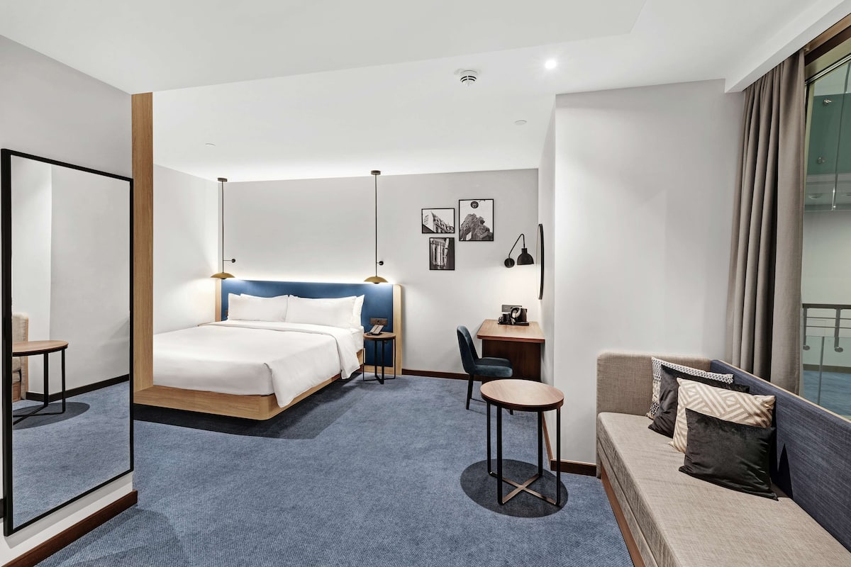 Moderni hotellihuone, jossa on suuri sänky, työpöytä, tuoli, pyöreä pöytä ja sohva.
