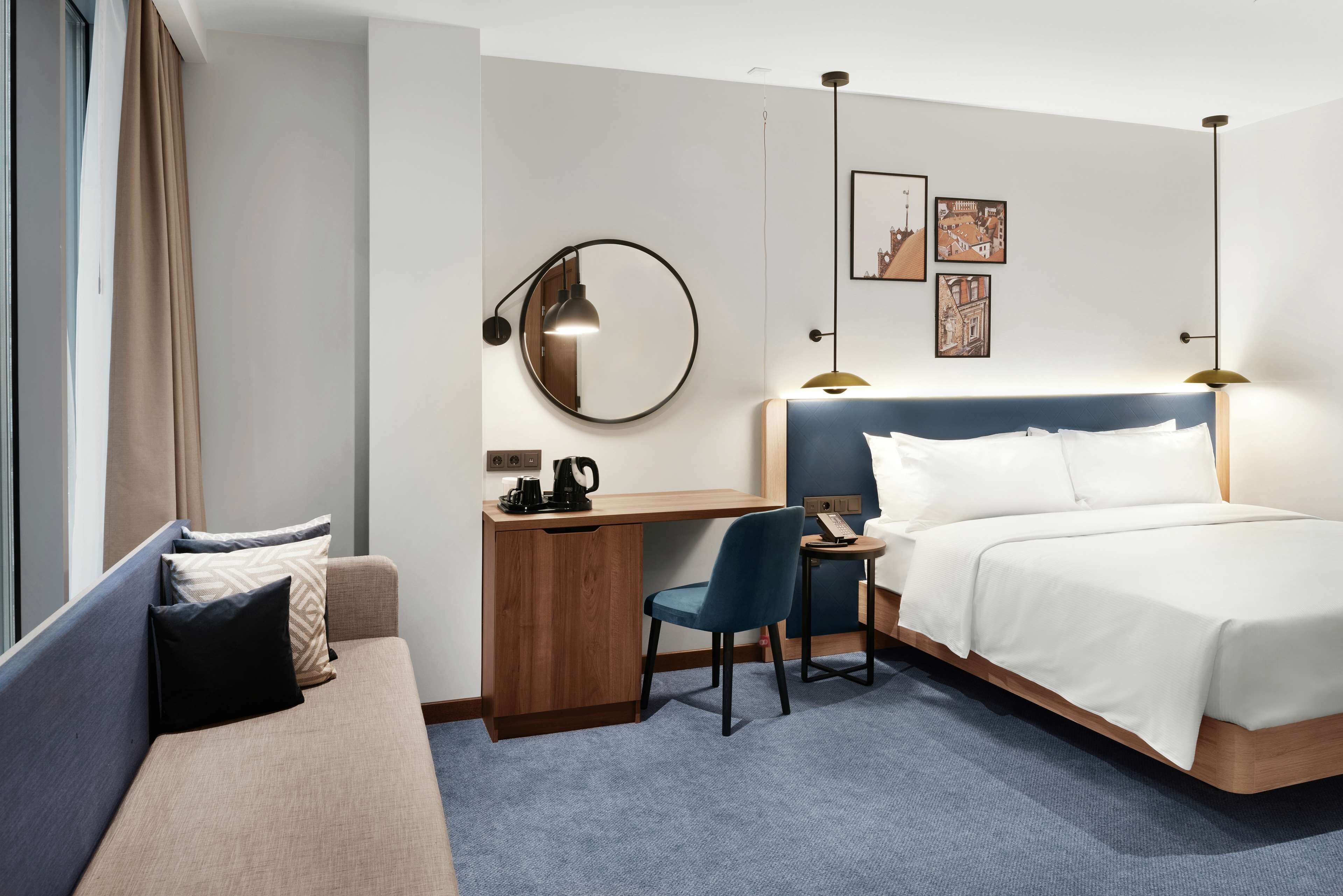 Une chambre d’hôtel équipée d’un lit, d’un bureau, d’une chaise, d’un canapé, d’un miroir rond et d’une machine à café.