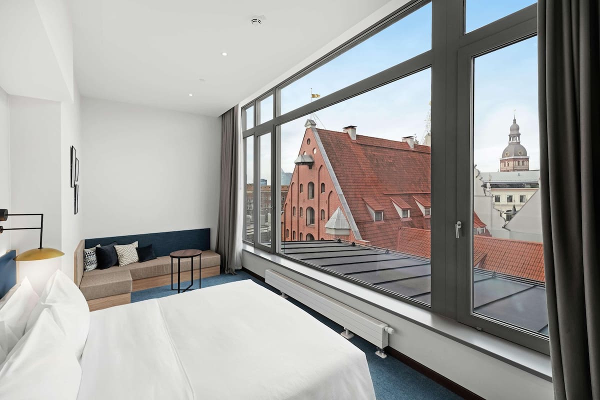 Moderni hotellihuone, jossa on suuri ikkuna, sänky, sohva ja pieni pöytä.