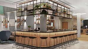 Un bar moderno con una barra curva, varios taburetes y un nivel superior con estanterías y plantas.