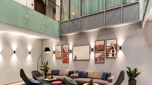 Un interior moderno con techo alto, paredes de vidrio, zona de estar con sofás y sillones, y obras de arte en las paredes.