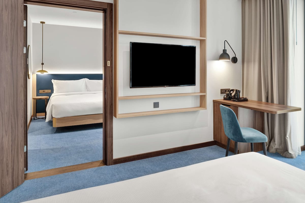 Hotellihuone, jossa on sänky, työpöytä tuolilla, seinälle asennettu televisio ja yöpöytä.