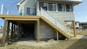 A multi-level wooden structure with a covered entrance, outdoor seating, and a fenced balcony. - Sounds Groovy OBX: Waterfront Home with Dock (Nags Head)