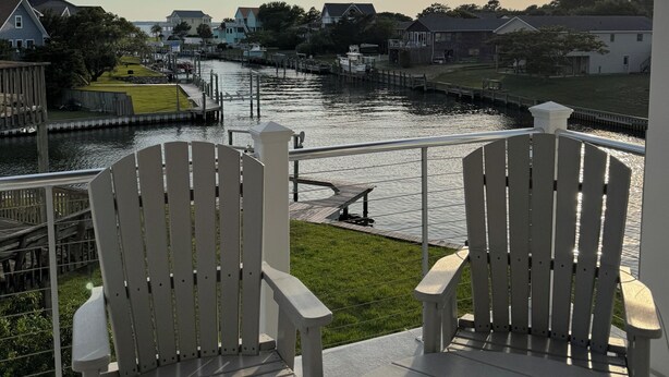 A deck with two Adirondack chairs overlooking a river with houses and a dock. - Sounds Groovy OBX: Waterfront Home with Dock (Nags Head)