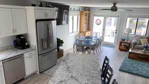 A modern kitchen with a built-in refrigerator, a coffee maker, and a dining area with a table and chairs. - Sounds Groovy OBX: Waterfront Home with Dock (Nags Head)