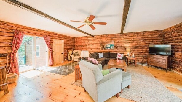 A cozy cabin-style room with wooden walls, a ceiling fan, a sofa, a TV, and a dining table. - Super Clean, Pet Friendly Cottage! 3 Bedroom! NO EXTRA FEES!! (Alexandria Bay)