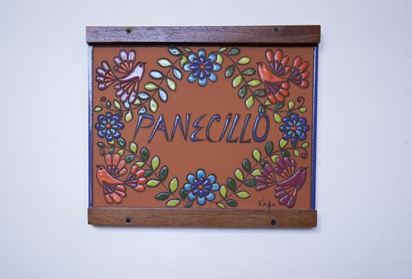Un letrero decorativo con diseños florales y de pájaros, que muestra el nombre 'PANECILLO'.