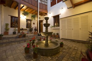 Un patio con una fuente de piedra, plantas en macetas y vigas de madera.