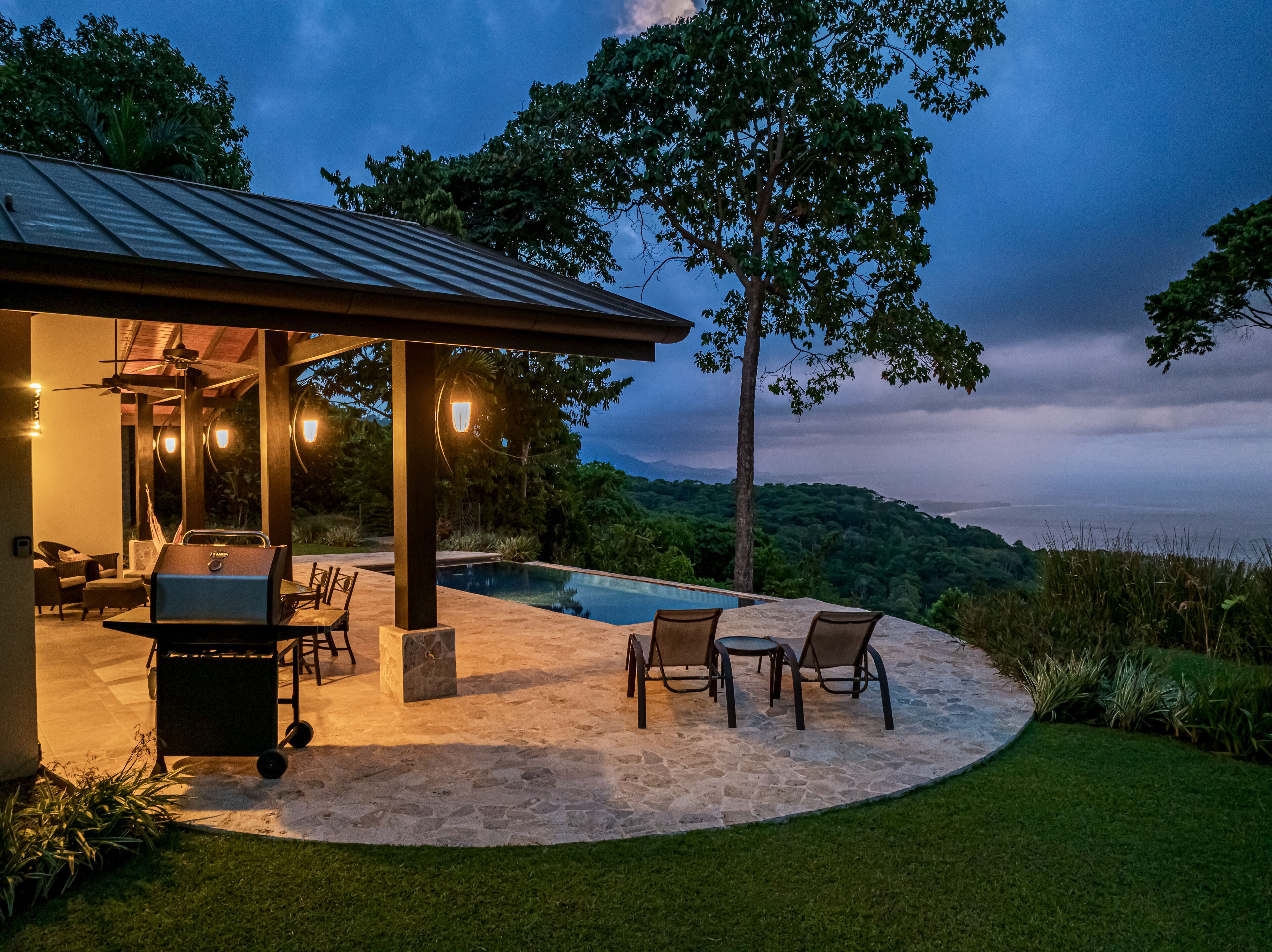 A covered outdoor area with a pool, seating, and grilling equipment.
