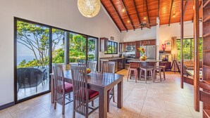 A spacious kitchen with large windows, a dining area with wooden furniture, and a view of the outdoors.